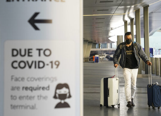 A sign displaying COVID-19 prevention protocols stands beside the passenger drop-off area as travelers arrive at Terminal C at LaGuardia Airport, Wednesday, Nov. 25, 2020, in the Queens borough of New York. Millions of Americans are taking to the skies and hitting the road ahead of Thanksgiving at the risk of pouring gasoline on the coronavirus fire. They are disregarding increasingly dire warnings that they stay home and limit their holiday gatherings to members of their own household. (AP Photo/John Minchillo)